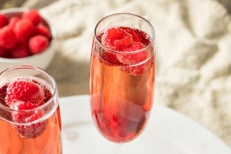 A glass of Kir Royale with raspberries in it